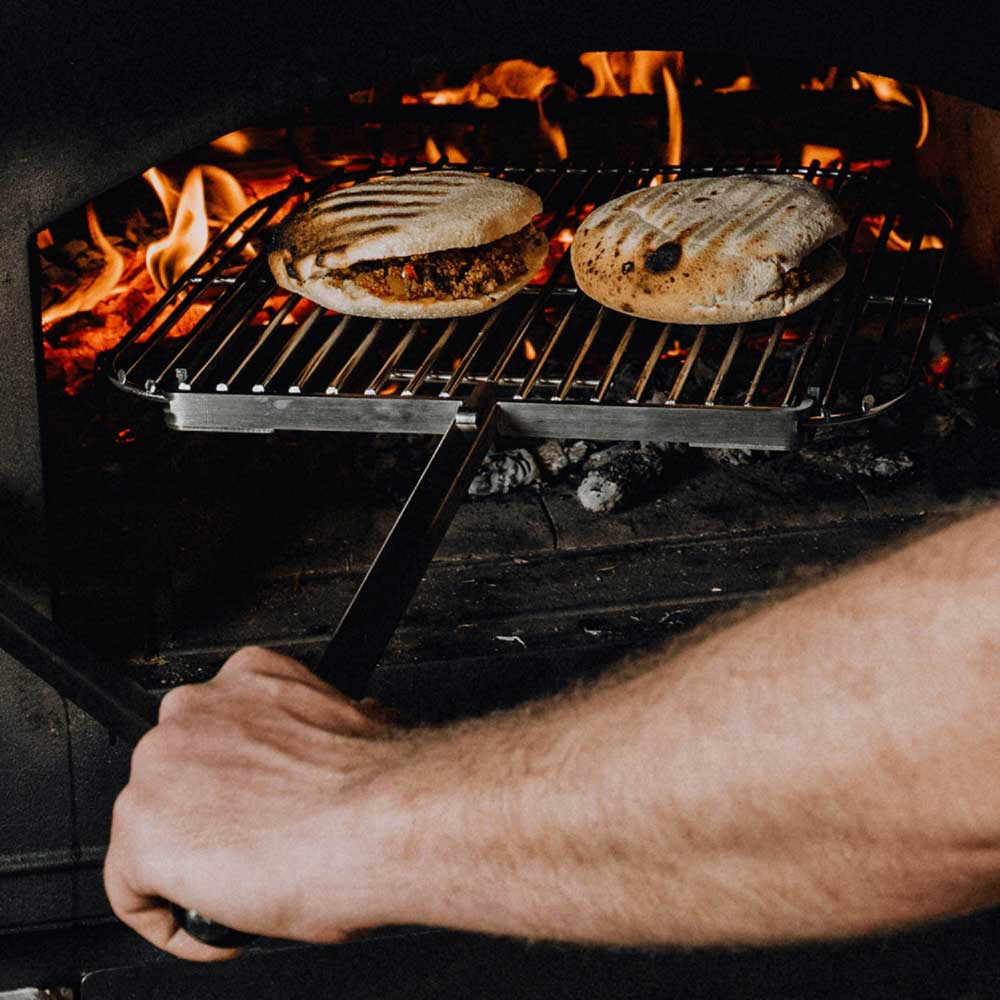 Grillschwenkarm belegt über offenem Feuer im Holzofen