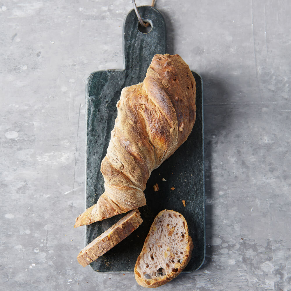 Rezept für Walnuss-Wurzelbrot knuspriges Walnuss-WUrzelbrot aufgeschnitten und auf einem schwarzen Holzbrett serviert