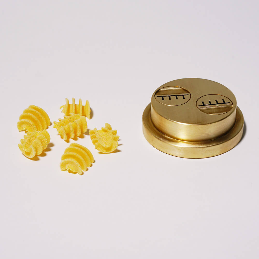 Matrize Nr. 260 - Radiatori Nudelmatrize Nr. 260 für Radiatori-Nudeln neben einigen Radiatori-Nudeln vor einem weißen Hintergrund.