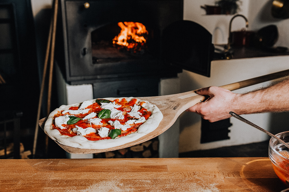 Belegte Pizza wird mit einem Holzschieber in einen traditionellen Häussler Holzbackofen eingeschossen.
