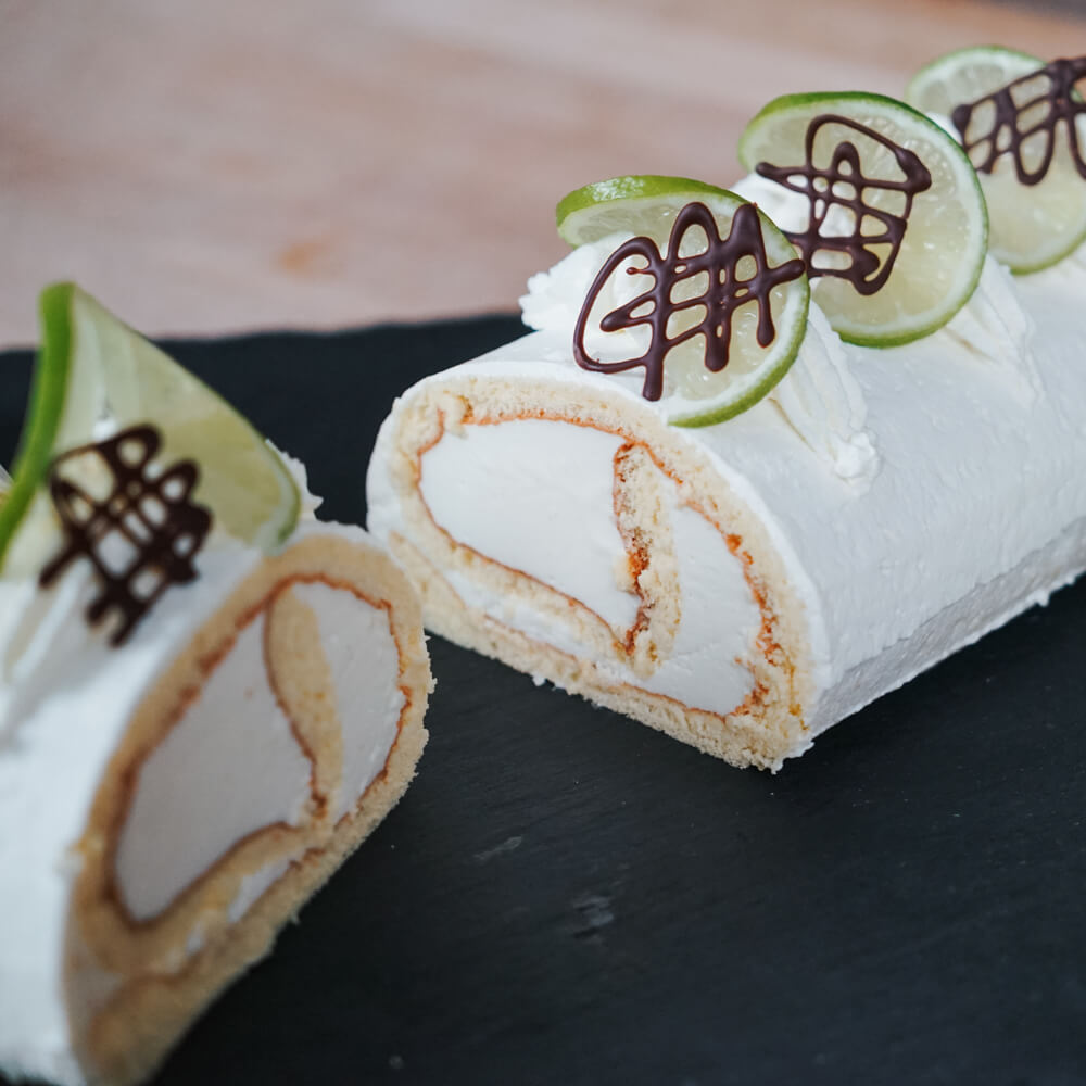 Rezept für Limetten Cheesecake Roulade eine Roulade gefüllt mit Limette und Sahne auf einer schwarzen Schieferplatte serviert