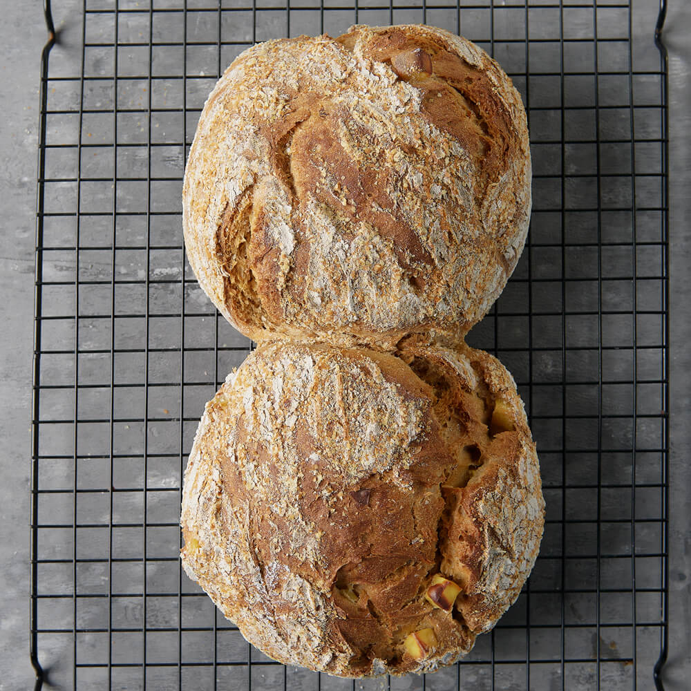 Rezept für Adelindes Würziges Kartoffelbrot 2 Kartoffelbrotlaibe auf einem schwarzen Gitter mit einem dunkelgrauen Hintergrund