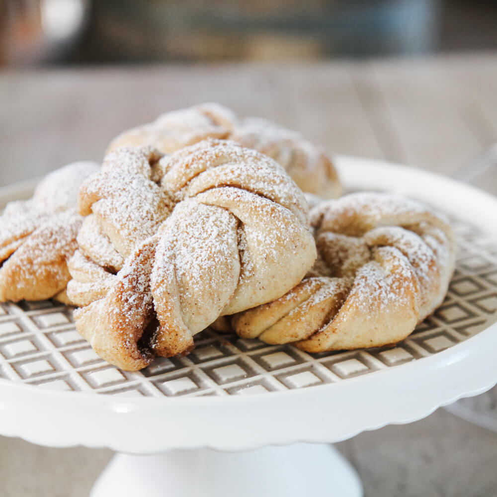 Rezept für Zimtknoten frisch gebackene Zimtknoten mit Puderzucker bestreut auf einer Servierplatte