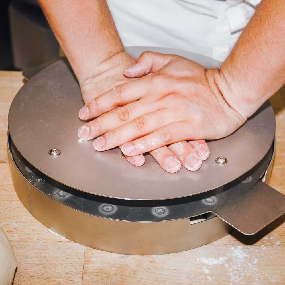 Teigteiler rund Eine Person drückt das Abstechwerkzeug in den runden, mit Teig gefüllten Teigteiler.