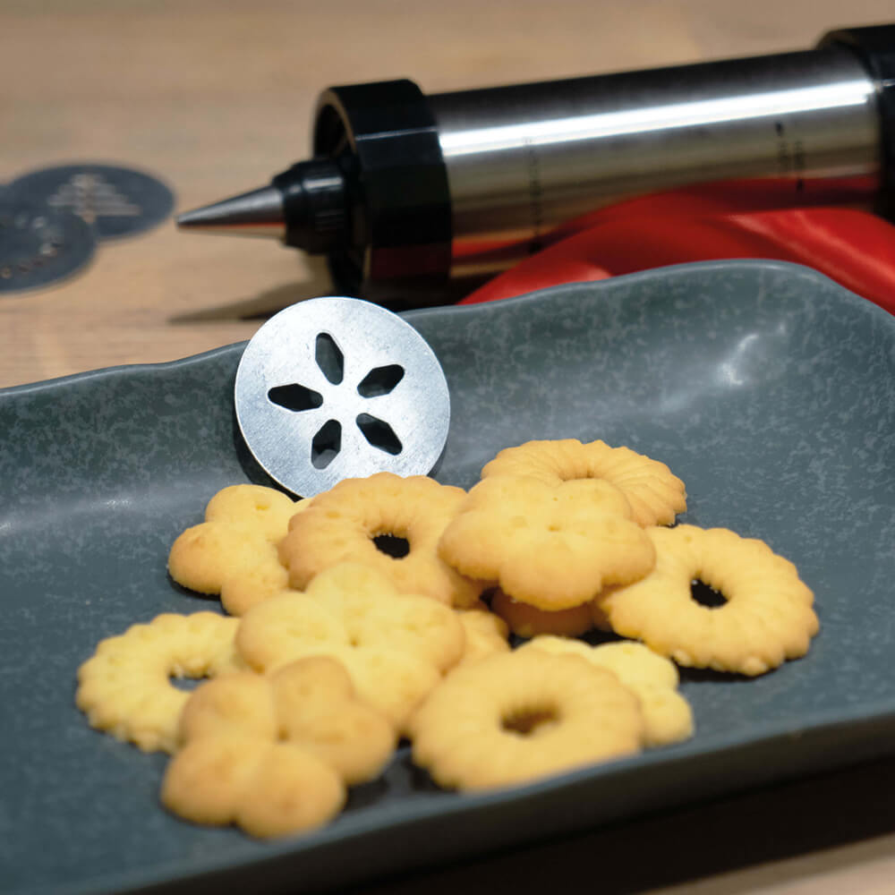 Gebäckpresse Verschiedene Gebäckformen auf einem dunkelgrauen Teller liegend. Im Hintergrund liegt eine Gebäckpresse.