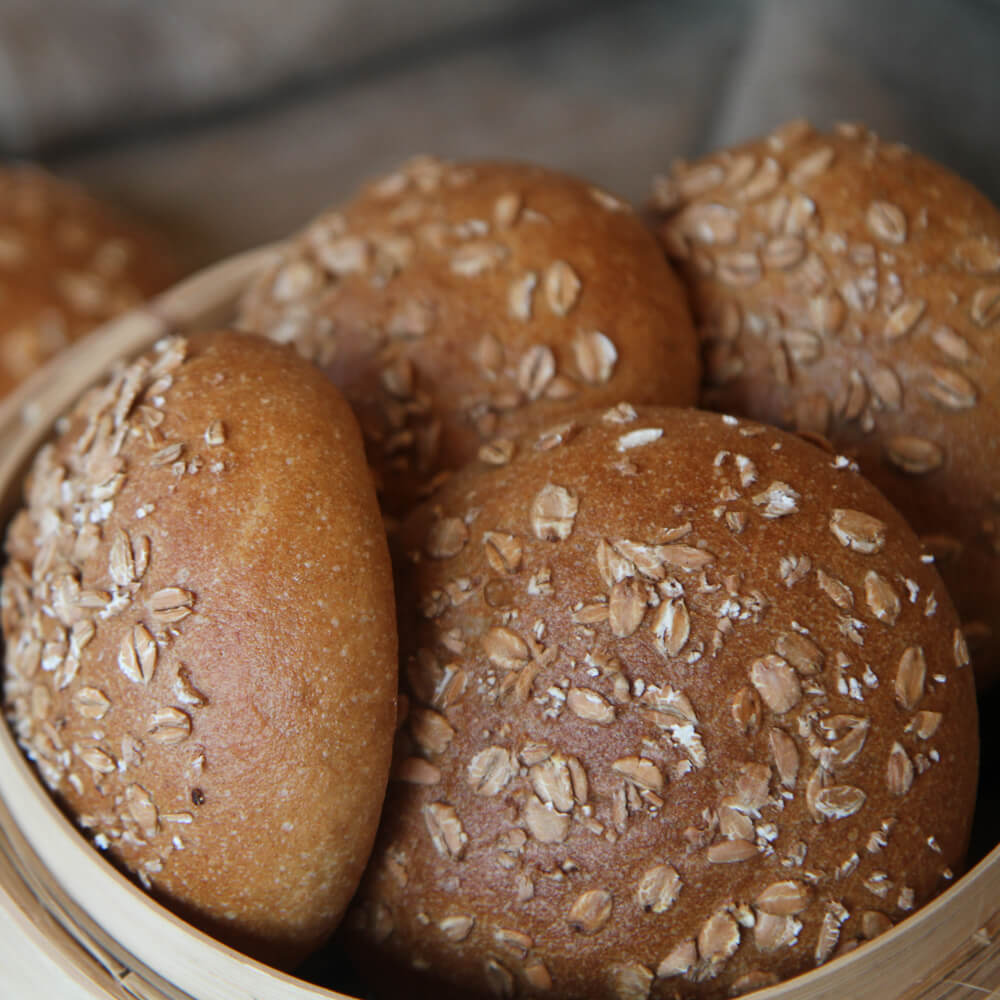 Rezept für Dinkel-Vollkornbrötchen mehrere Dinkel-Vollkornbrötchen in einem Brotkorb aus Holz, bestreut mit ein paar Haferflocken