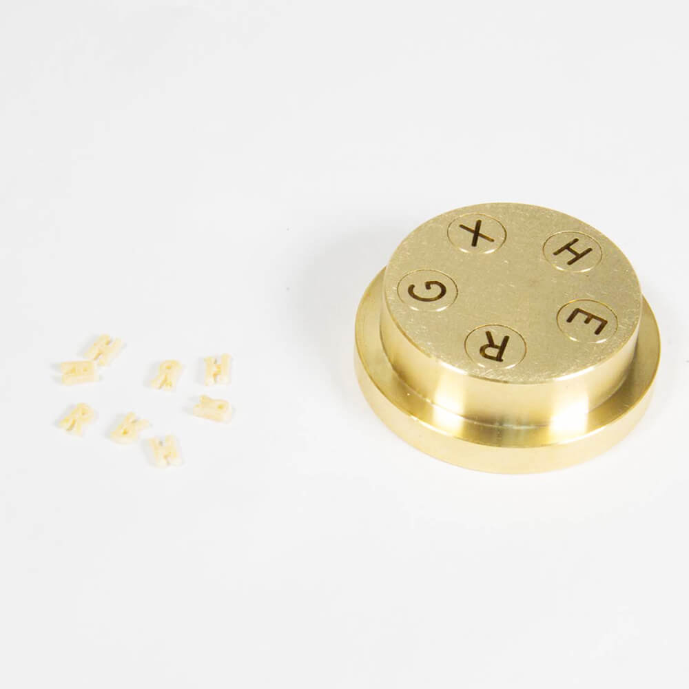 Matrize Nr. 330 - Pasta alphabeto Nudelmatrize Nr. 330 für Buchstaben-Nudeln neben einigen Buchstaben-Nudeln vor einem weißen Hintergrund.