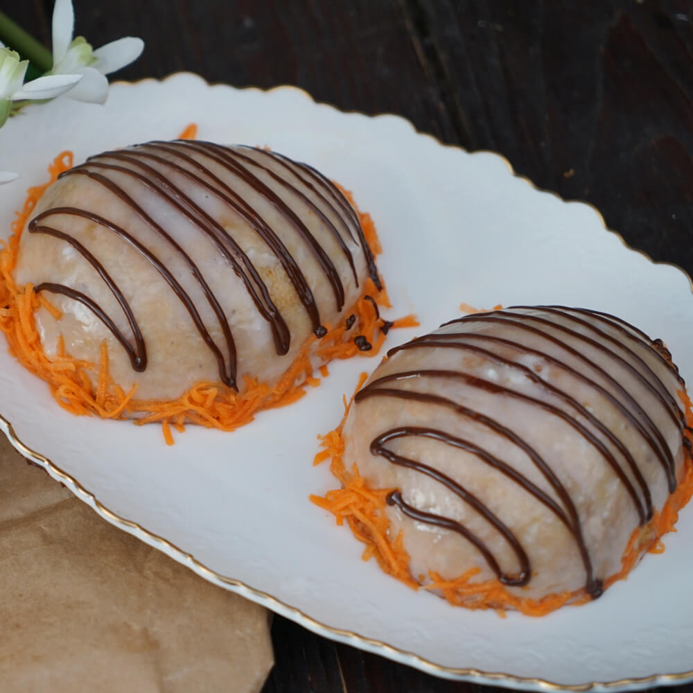 Rezept für Rübli-Eier 2 Rübli-Ei Hälften, eingestrichen mit Zuckerguss und dekoriert mit Schokolade und frisch geraspselten Karotten auf einer weißen Tortenplatte serviert