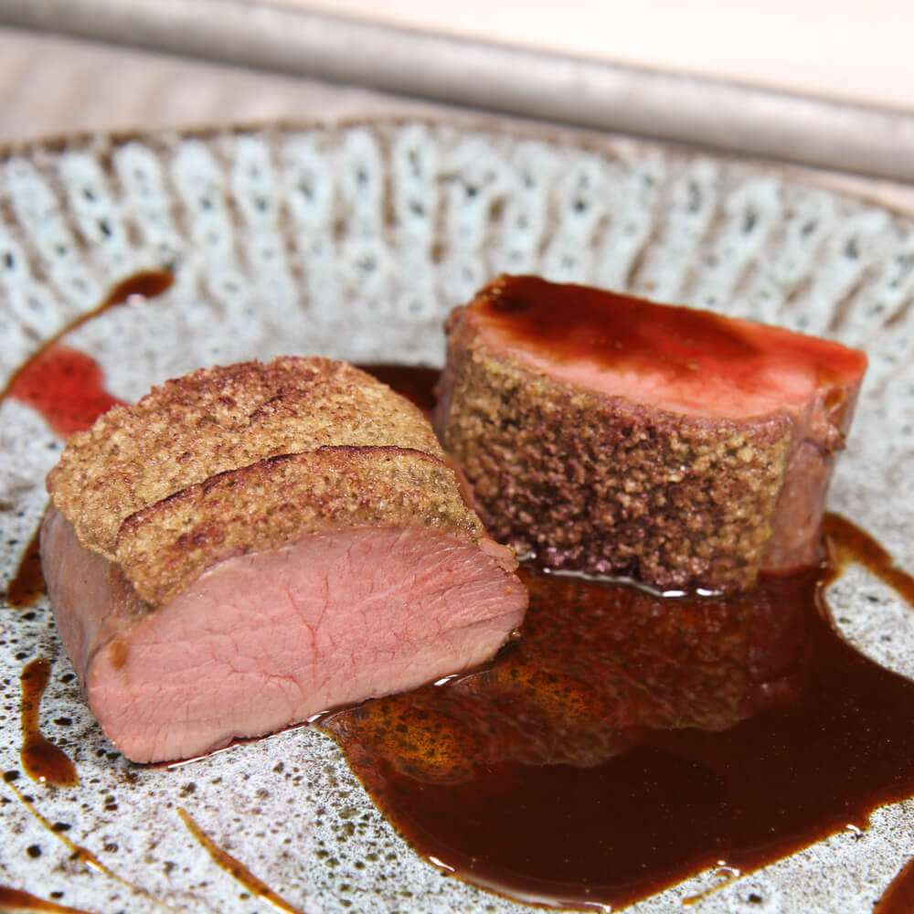 Rezept für Rehrücken mit Nusskruste rosa gebratener Rehrücken mit Nusskruste und einer Soße auf einem hellen Teller serviert