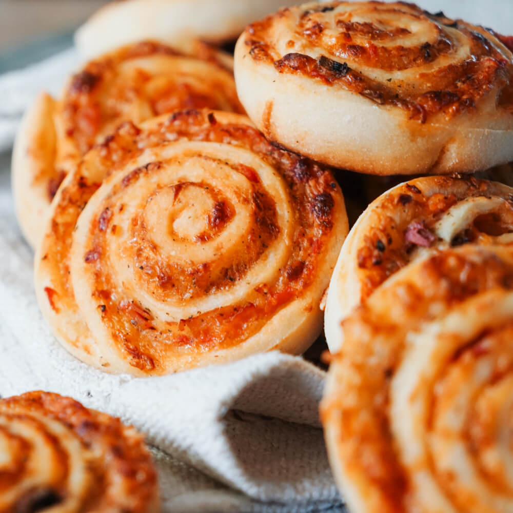 Rezept für Pizzaschnecken saftige Pizzaschnecken mit Tomatensoße und Käse auf einem grauen Tuch