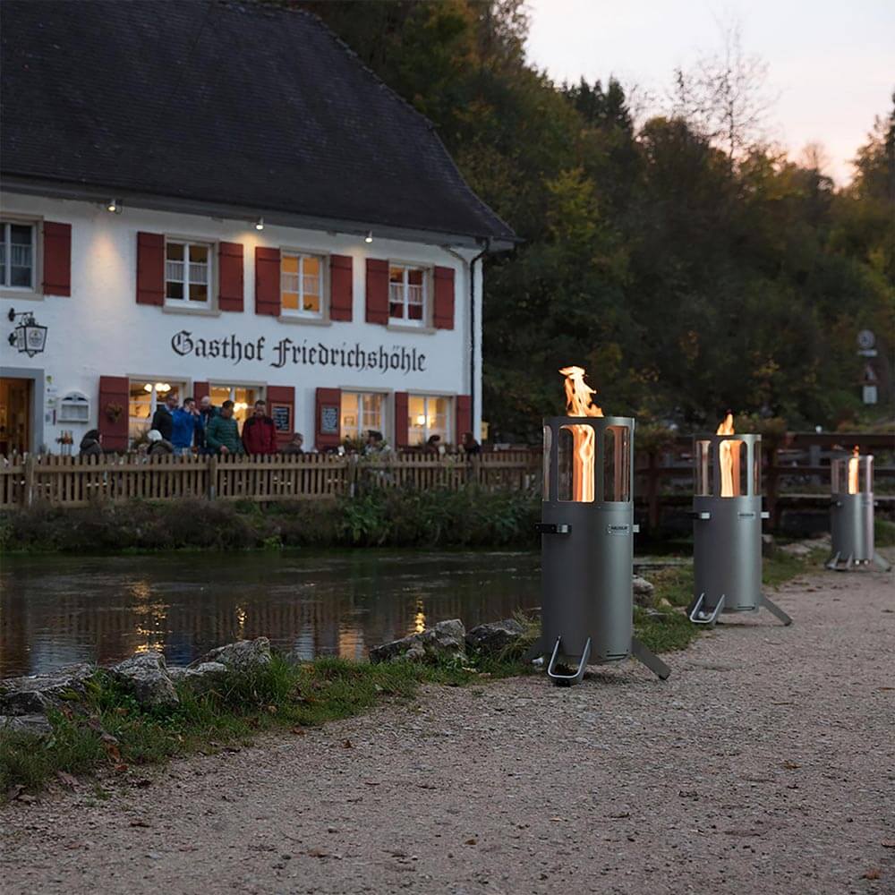 Drei Ambientelichter mit angezündetem Feuer an einem Fluss entlang bei Dämmerung.