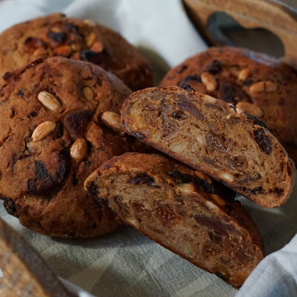 Rezept für Früchtebrot Glutenfrei selbstgemachtes glutenfreies Früchtebrot mir Nüssen und Dörrobst in einem Holztablett mit grauem Geschirrtuch serviert