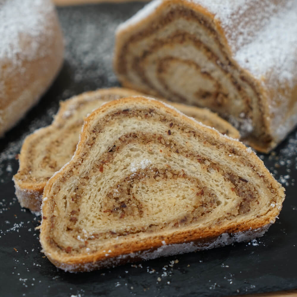 Rezept für Nussstollen Nussstollen in der typischen Stollenform mit Puderzucker bestreut und aufgeschnitten auf einer Schieferplatte