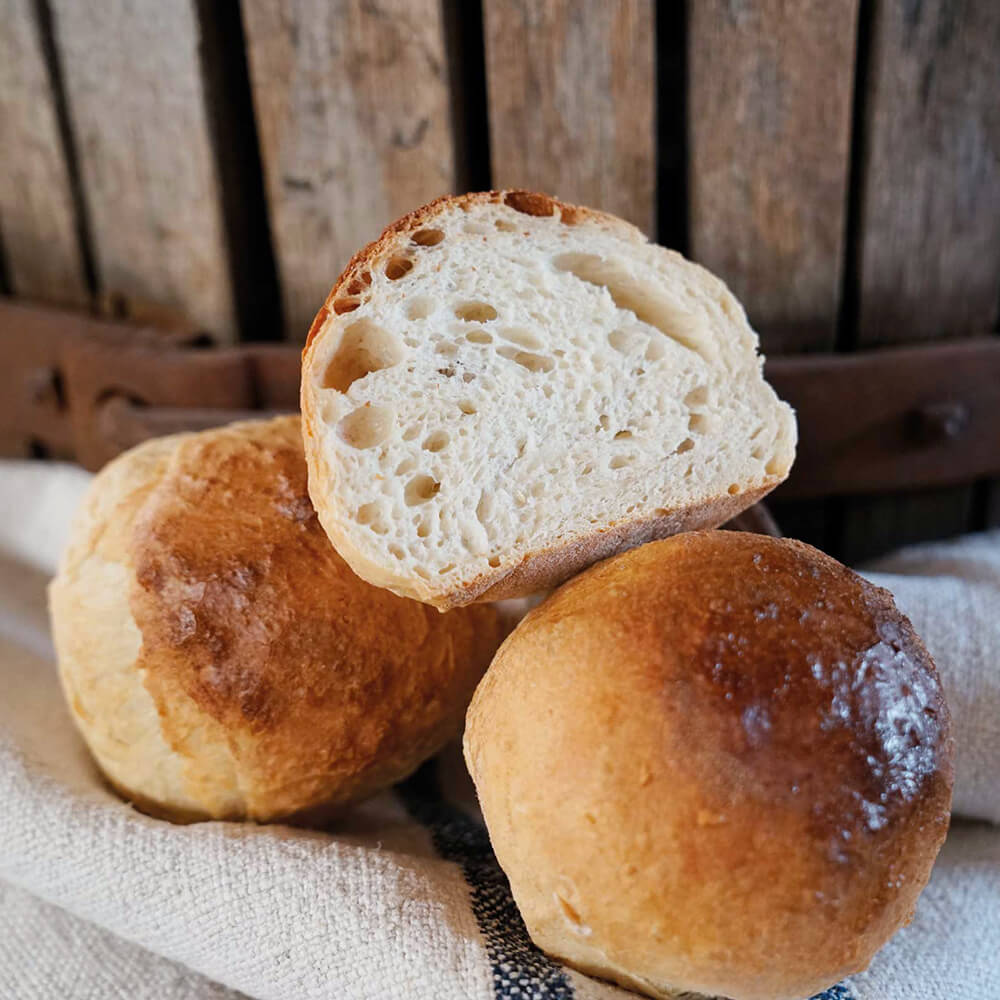Knauzenschießer 3 Brötchen, davon eines in der Mitte aufgeschnitten, liegen auf einem Stofftuch und im Hintergrund befindet sich ein Holzfass