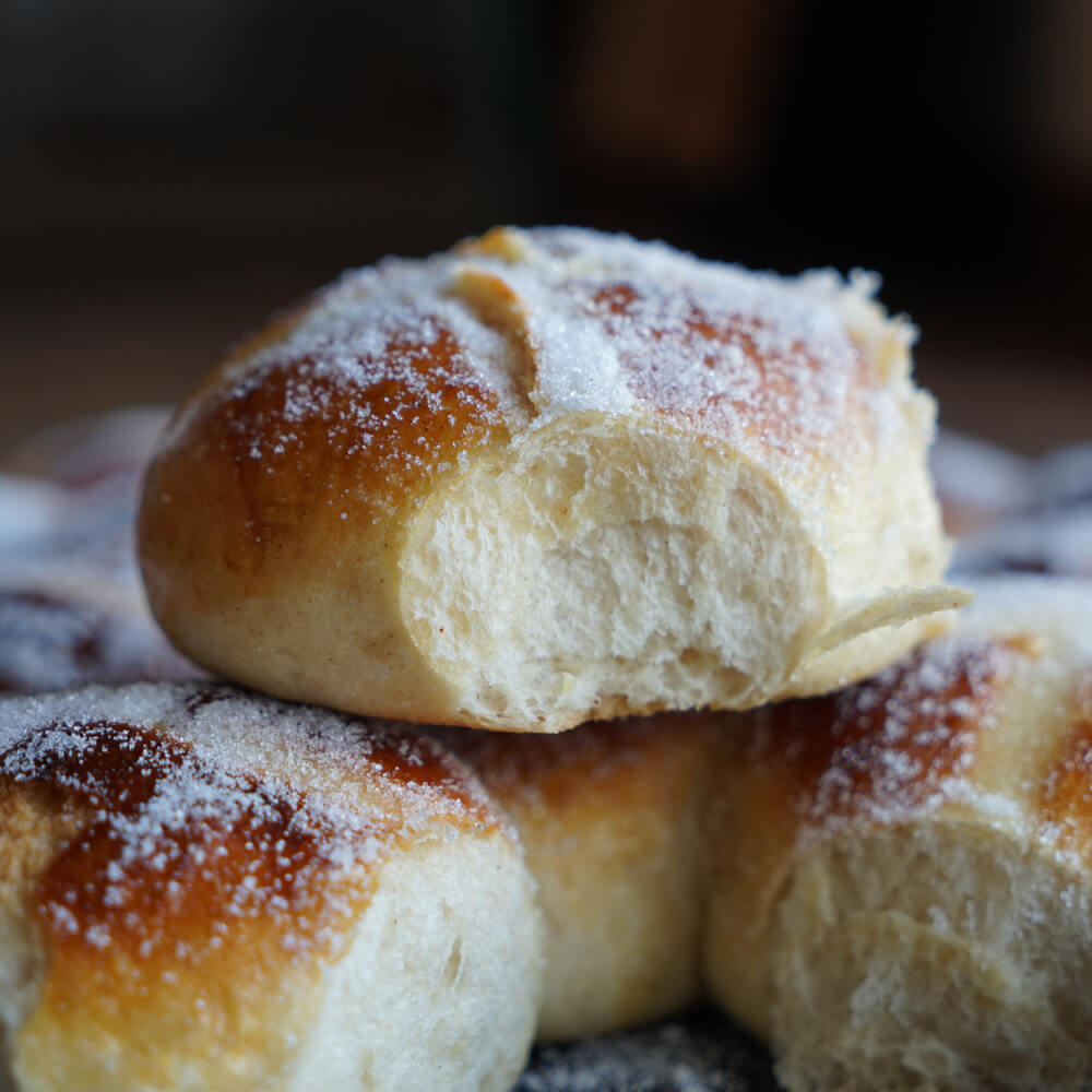 Rezept für Hot Cross Buns leckes Hefegebäck in Brötchenform mit einem Kreuz drauf und mit Zucker bestreut vor einem dunklen Hintergrund