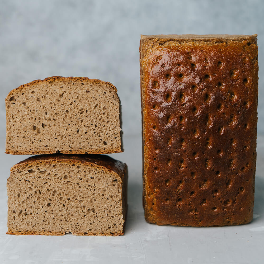 Paderborner Landbrot aufgeschnittenes und ganzes gestipptes Paderborner Landbrot nebeneinandern. Grauer Hintergrund
