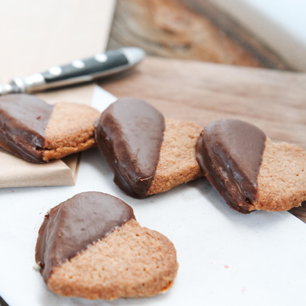 Rezept für Emmer-Linzerplätzchen Emmer Linzerplätzchen in Herzform mit Marmeladenfüllung und Schokoglasur auf einem Backbrett serviert