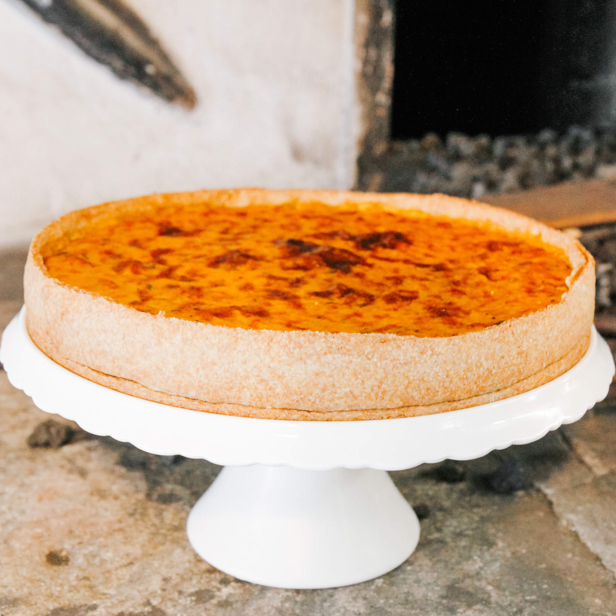 Rezept für Kürbisquiche selbstgemachte Kürbisquiche auf einer weißen Tortenplatte serviert.