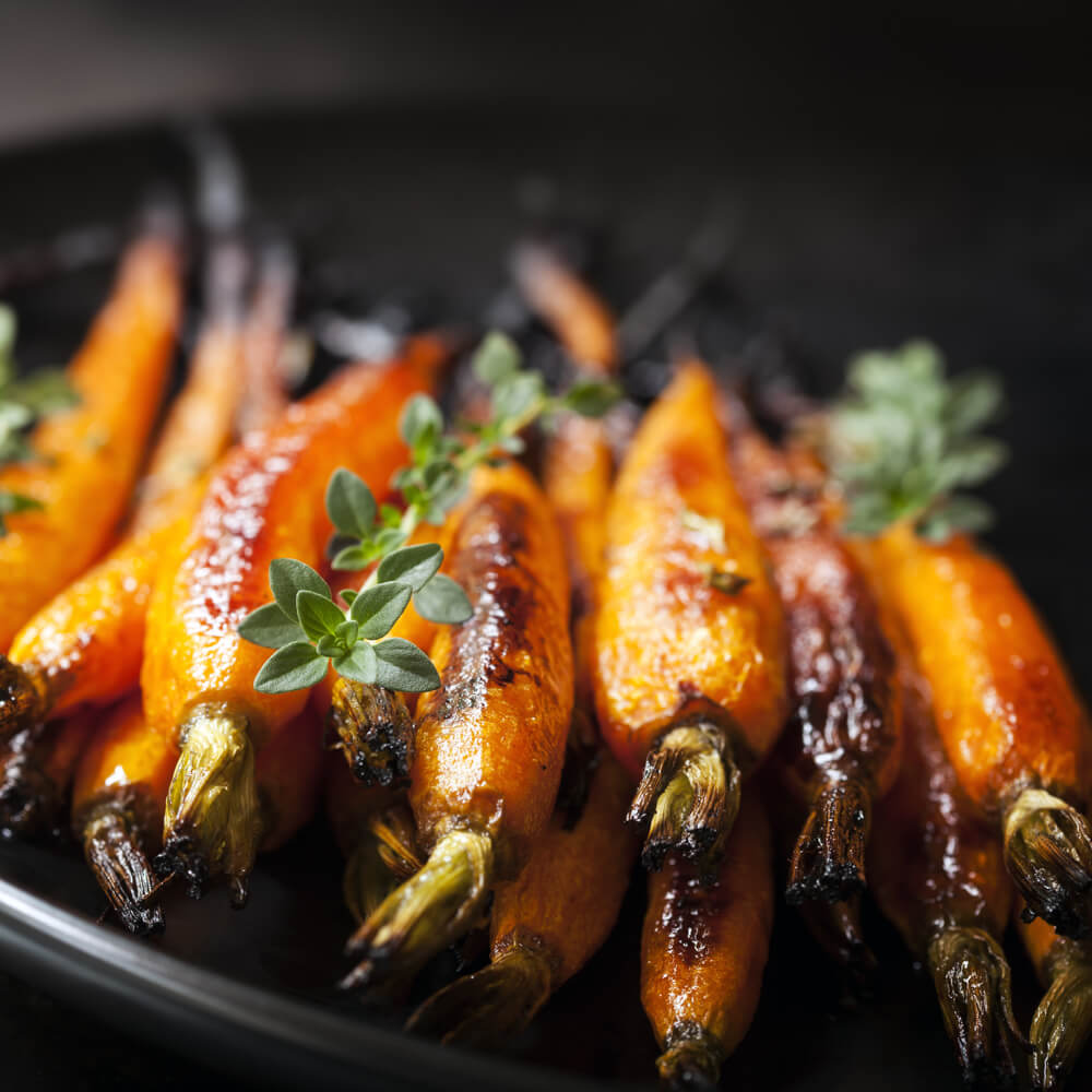 Rezept für Glasierte Möhren frische glasierte Möhren in einer schwarzen Schüssel mit Thymian garniert