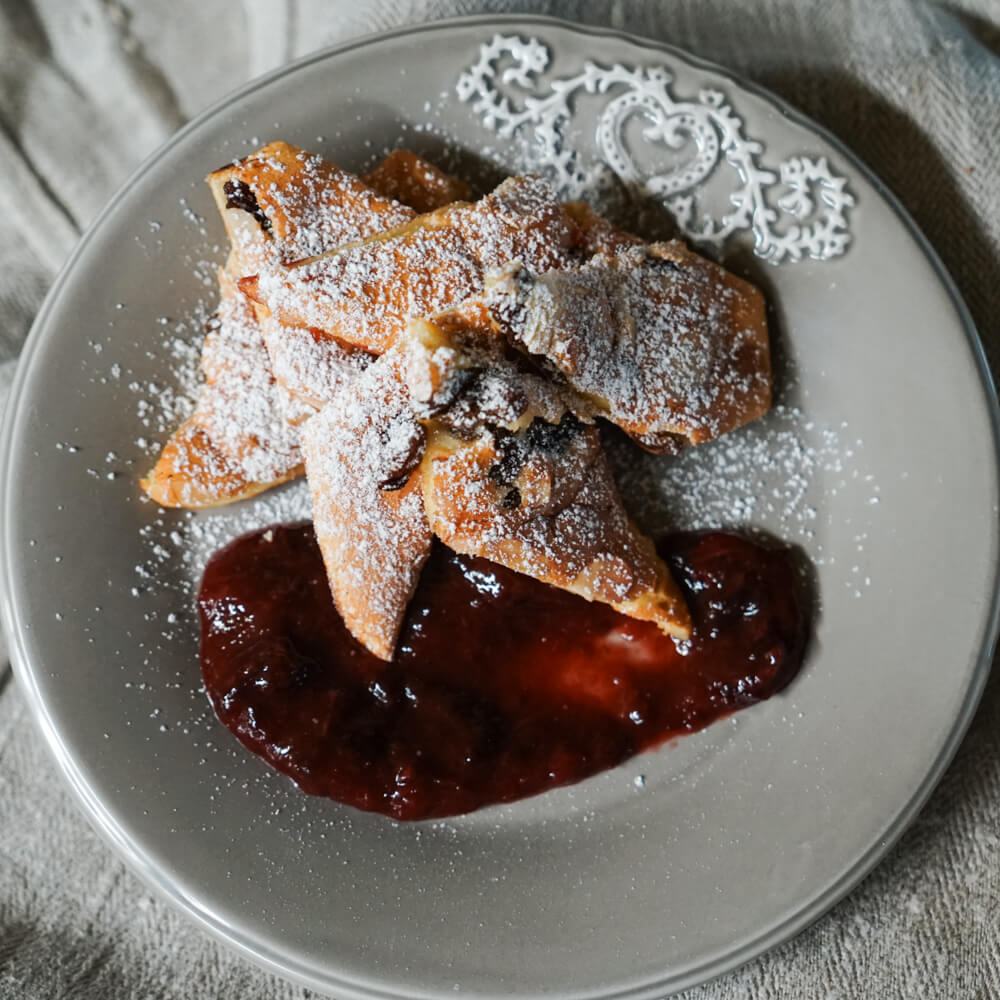 fluffiger Kaiserschmarrn mit Zwetschegenkompott und Puderzucker auf einem grauen Teller serviert